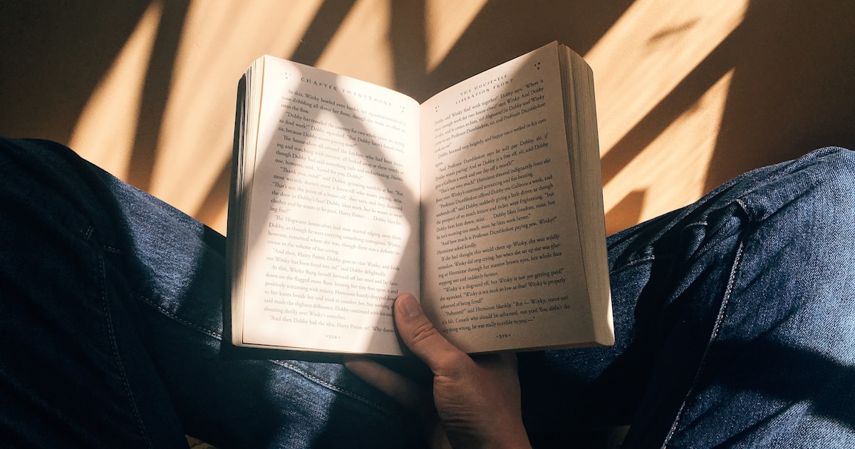 person holding book sitting on brown surface